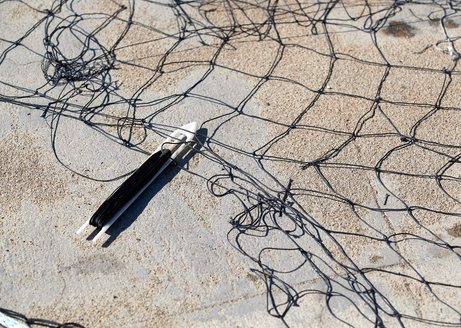 Twine Wrapped Around a Netting Needle Next to a Fishing Net